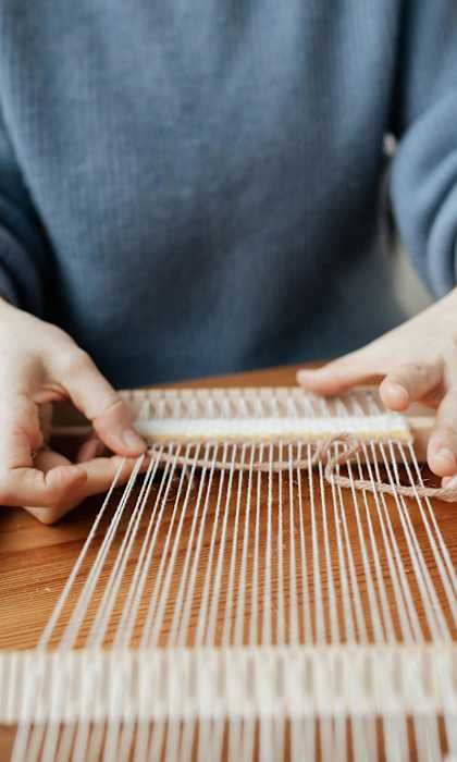 A person is weaving a piece of fabric on a wooden loom.