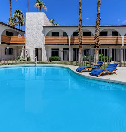 a swimming pool with blue chaise lounges and a building in the background