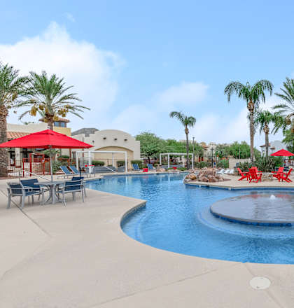 A pool surrounded by palm trees and red umbrellas.