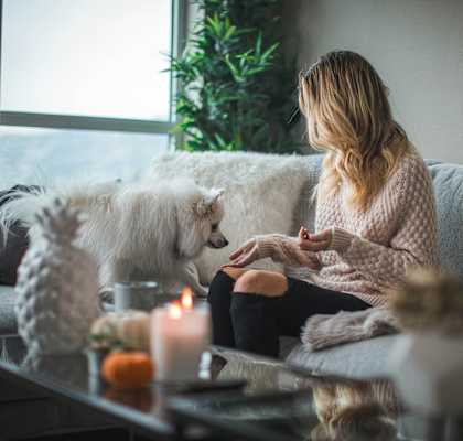 A woman is sitting on a couch with a dog beside her, looking at her phone.