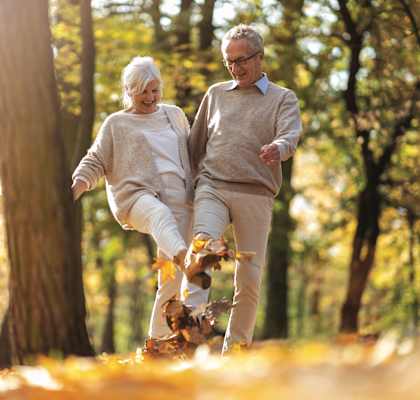 An older couple walking through the autumn leaves