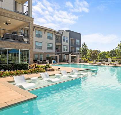 A large swimming pool with lounge chairs and apartment buildings in the background.