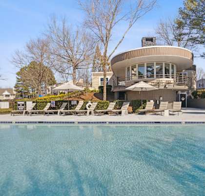 a swimming pool with chairs and a house in the background
