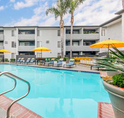 a swimming pool with yellow umbrellas in front of an apartment building