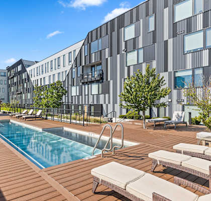 A pool area with sun loungers and a modern building in the background.
