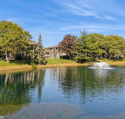 A serene lake with a fountain in the middle surrounded by trees and buildings at Island Club Apartments, Columbus, OH, 43235