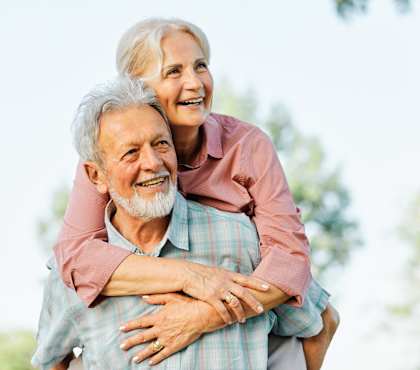 An older man is giving a piggyback ride to a woman outdoors.
