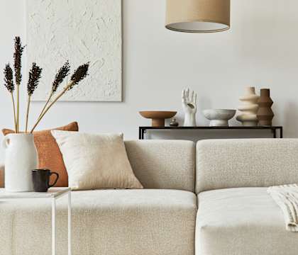 A living room with a white couch and a vase with dried flowers on a small table.