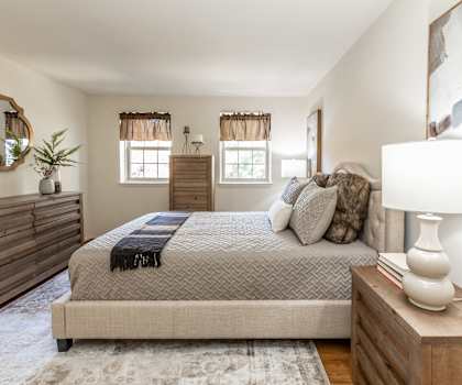 A bedroom with a large bed, a wooden dresser, and a rug on the floor.at The Orchards at Severn Townhomes*, Severn