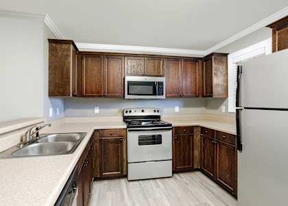 kitchen with a refrigerator, microwave, stove, and brown wooden cabinets at The Meadows Apartments in Florence, AL