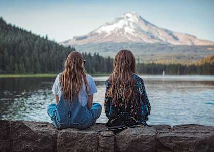 two women sitting on a rock overlooking a lake and a mountain