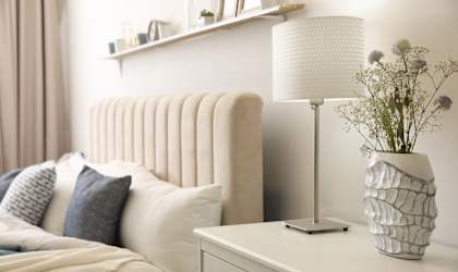 A white lamp stands on a nightstand next to a vase with flowers.