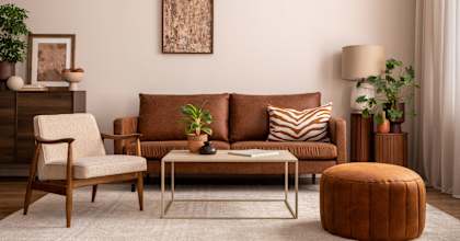 A living room with a brown couch, a chair, a coffee table, and a potted plant.