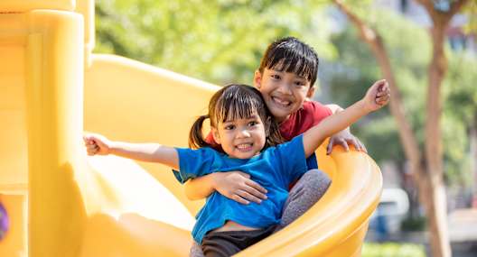 Two children are playing on a yellow slide.