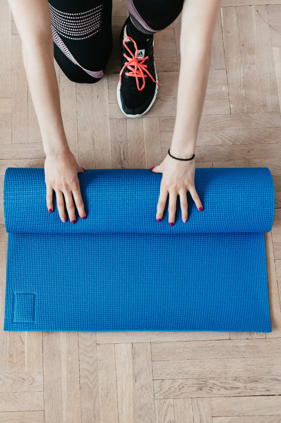 a woman sitting on a blue yoga mat on the floor next to dumbbells