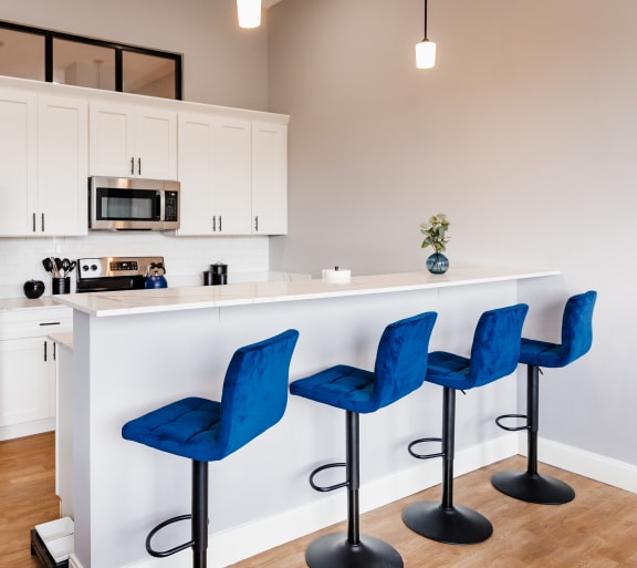 a living room with a kitchen in the background and a glass table and chairs in the foreground
