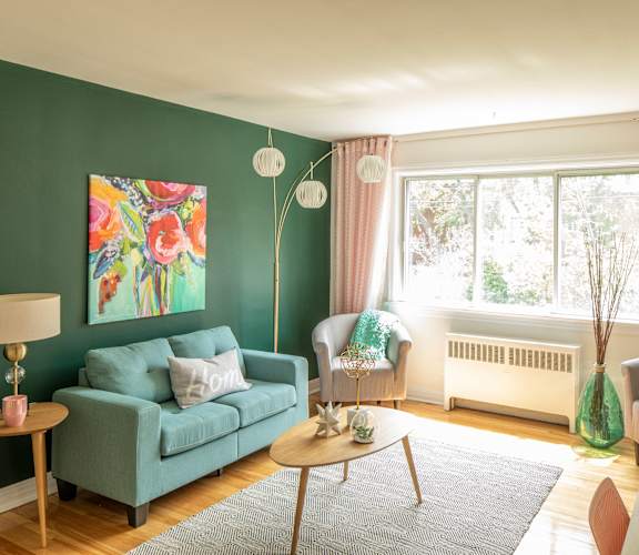 A living room with a green couch, a table with a lamp, and a painting on the wall.