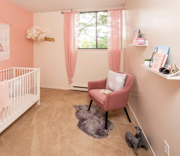A baby nursery with a pink theme, featuring a white crib, a pink chair, and a grey stuffed animal.