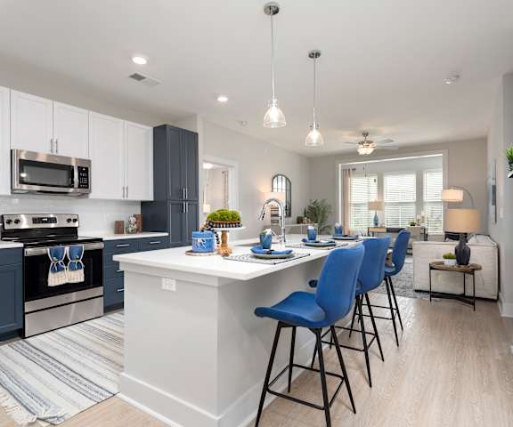 an open kitchen and living room with a large island and blue chairs at Bristol at New Riverside, Bluffton, SC