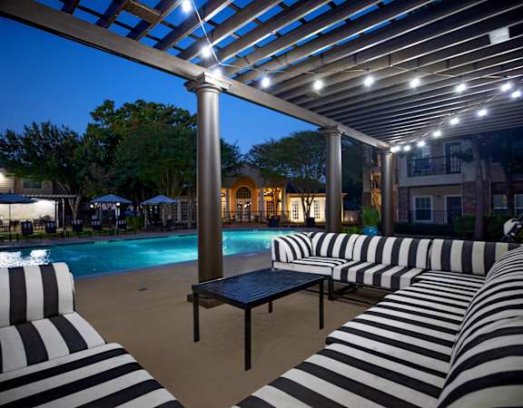 a swimming pool with black and white striped lounge chairs and umbrellas at night