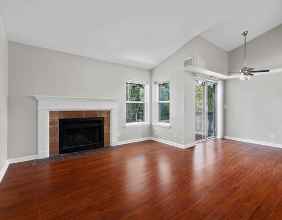 A large empty room with a fireplace and wood flooring.