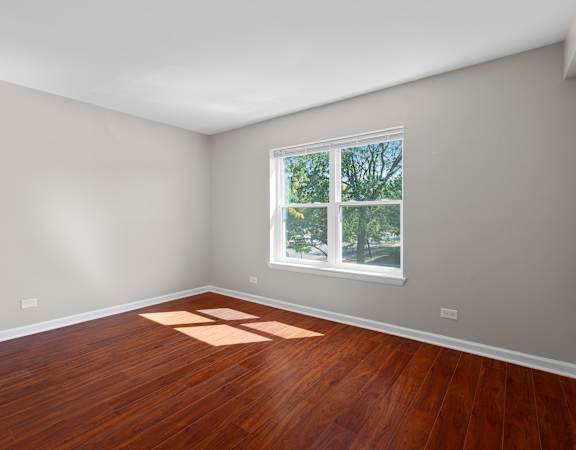 A room with wooden floors and a window showing trees outside.