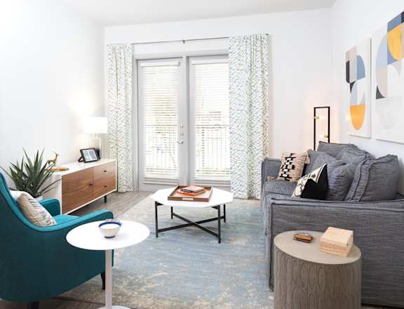 A living room with a blue armchair, a grey couch, a coffee table, and a painting on the wall.