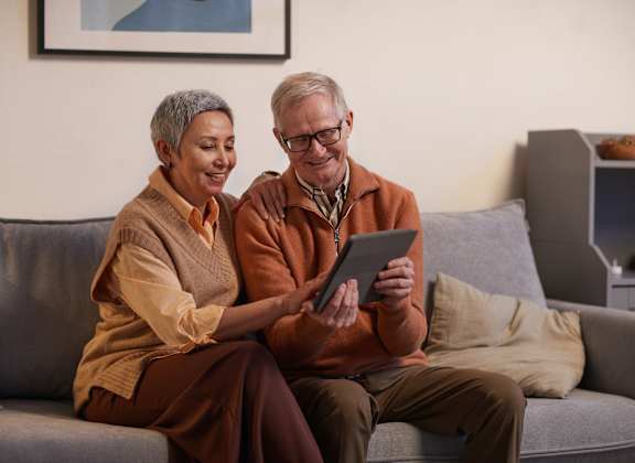 an older couple sitting on a couch looking at a tablet