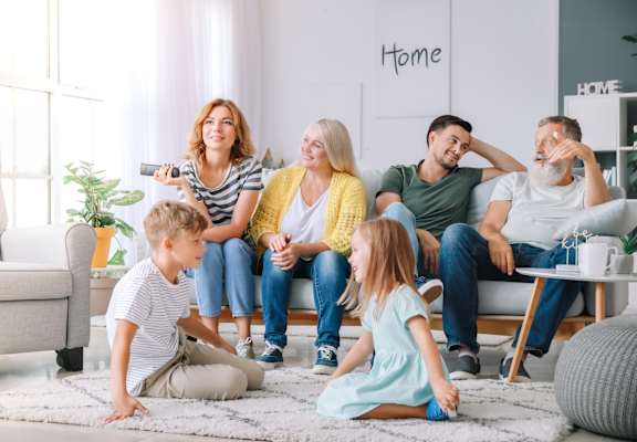 A family of six is sitting on the floor in their living room.