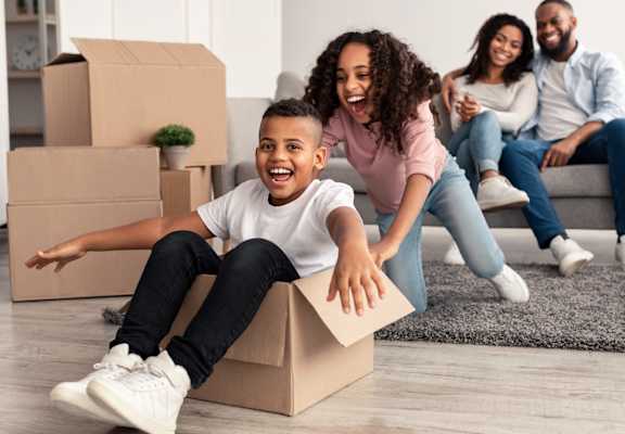 A person is sitting in a cardboard box in a room with other people sitting on a couch.
