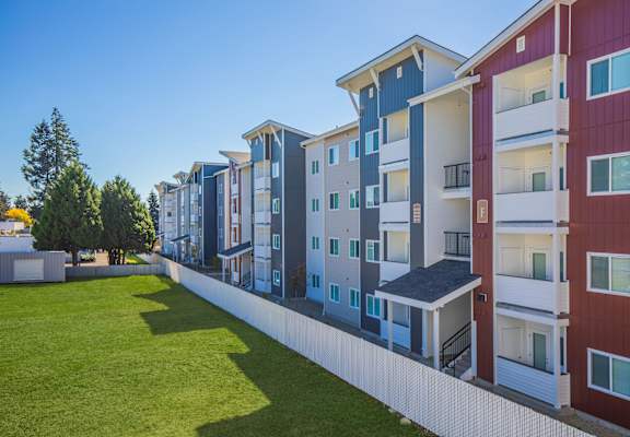 A row of modern apartment buildings with balconies and a green lawn in front.