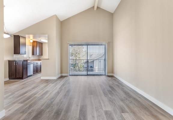 an empty living room with a door to a balcony and a kitchen