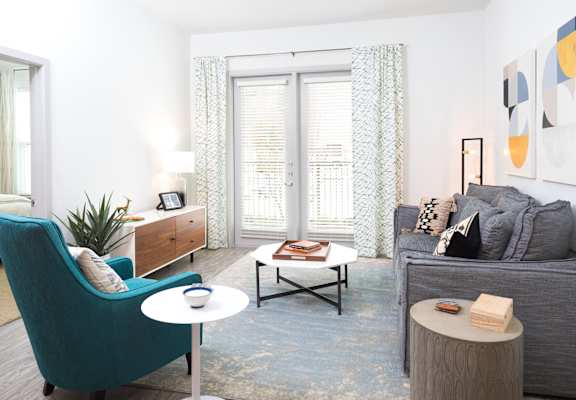 A living room with a blue armchair, a grey couch, a coffee table, and a painting on the wall.