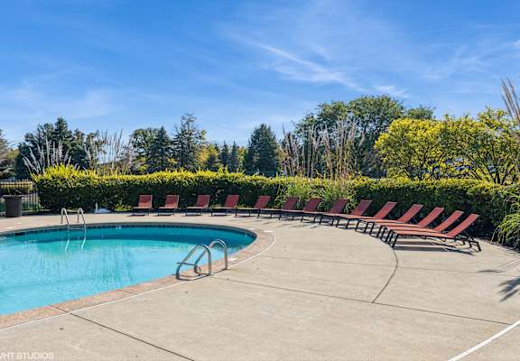 A pool surrounded by red lounge chairs and green trees at Island Club Apartments, Columbus, OH