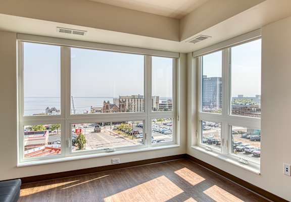 A room with a view of a parking lot and buildings outside the window.