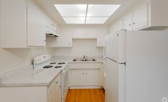 A small, white kitchen with a stove, sink, and refrigerator.