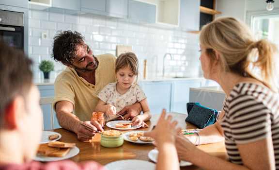 A family of four is having a meal together at the kitchen table.