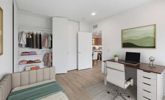 A room with a couch, a desk, and a closet with clothes.