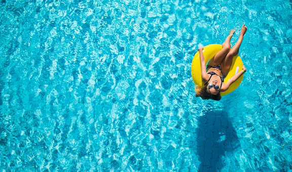A woman in a yellow swim ring is floating in a pool.