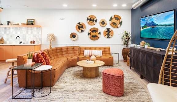 A living room with a brown sofa, a coffee table, and a TV on the wall. at The Reserve La Mirada, California