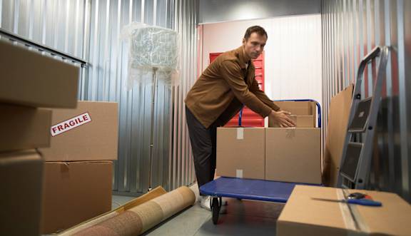 A man is moving boxes in a room with corrugated metal walls.