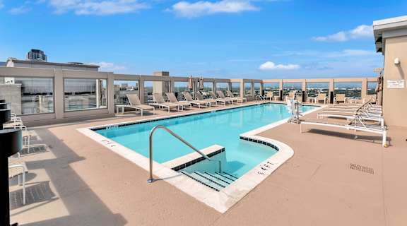 the pool on the rooftop of a building with chairs and a blue sky