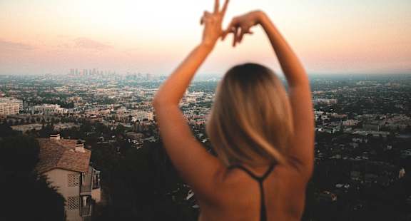 A woman with her back to the camera is making a peace sign with her hands at The Marquee Apartments, North Hollywood, California