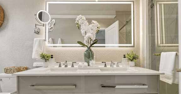 A bathroom vanity with a mirror, sink, and a vase of white flowers.