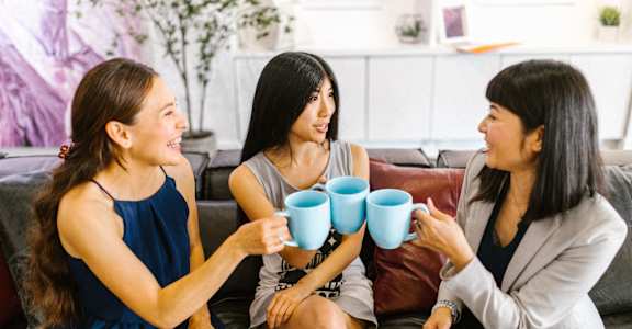 three women sitting on a couch drinking coffee
