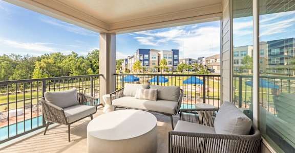 A balcony with a white couch, grey armchair, and a white ottoman.