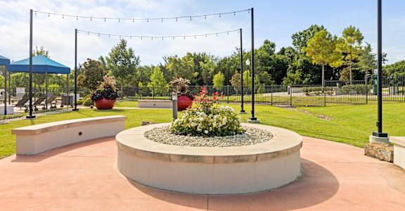 A garden with a circular flower bed in the center and string lights above.