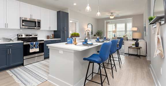 an open kitchen and living room with a large island and blue chairs at Bristol at New Riverside, Bluffton, SC