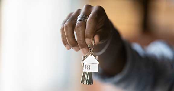 A person holding a set of keys with a keychain that has a house keyring attached to it.