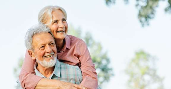 An older man is giving a piggyback ride to a woman outdoors.